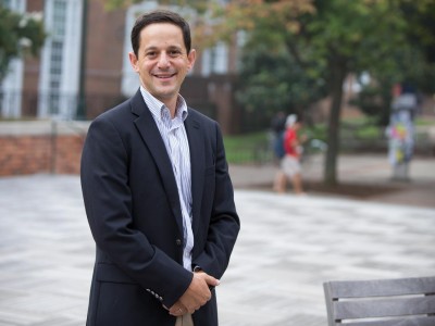 Man in a blue blazer and white shirt standing in front of a brick building