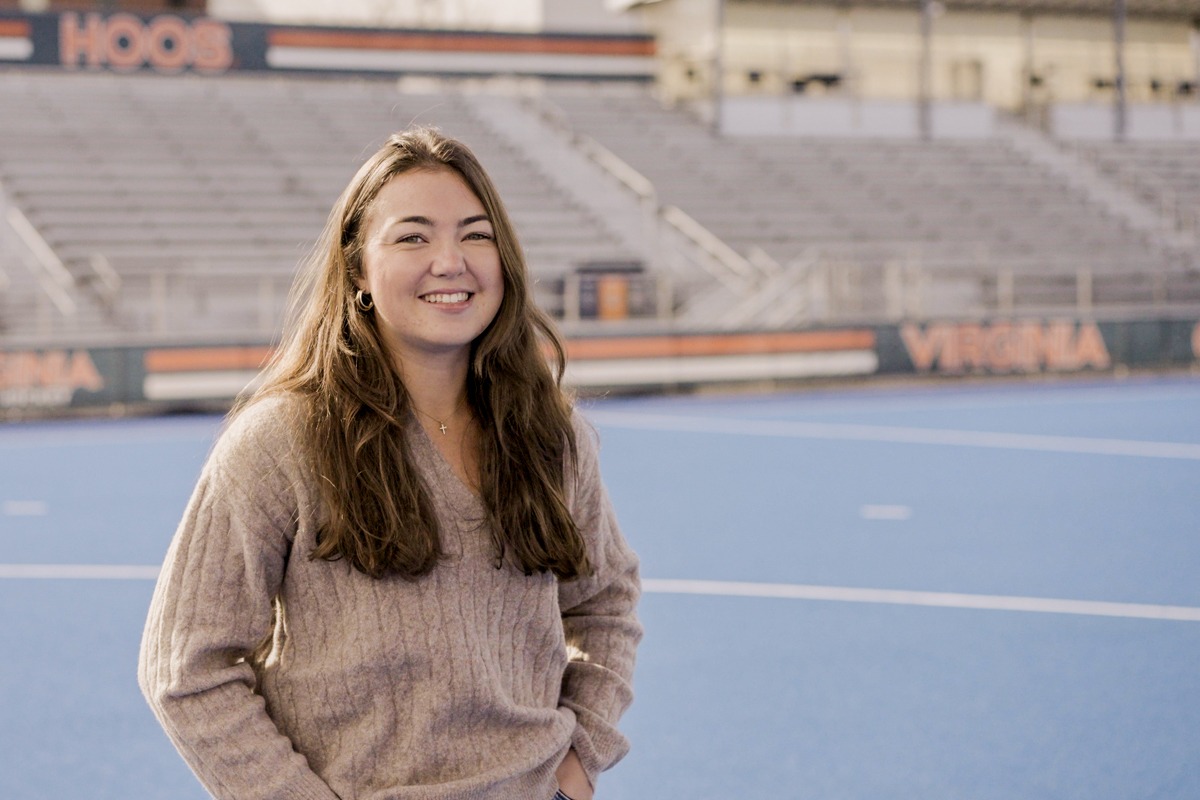 UVA Batten student Mia Abello is smiling, standing in the middle of the UVA Field Hockey stadium