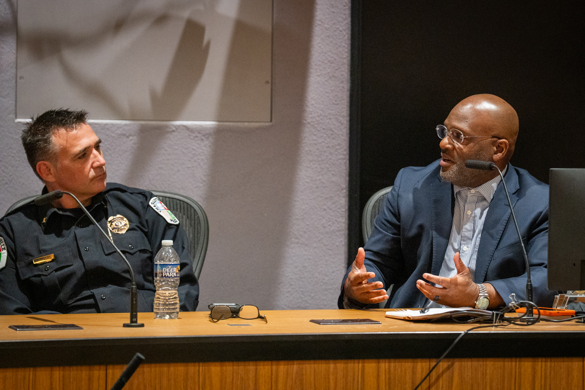 A man on the left in a police uniform listens to another member of the panel speaking