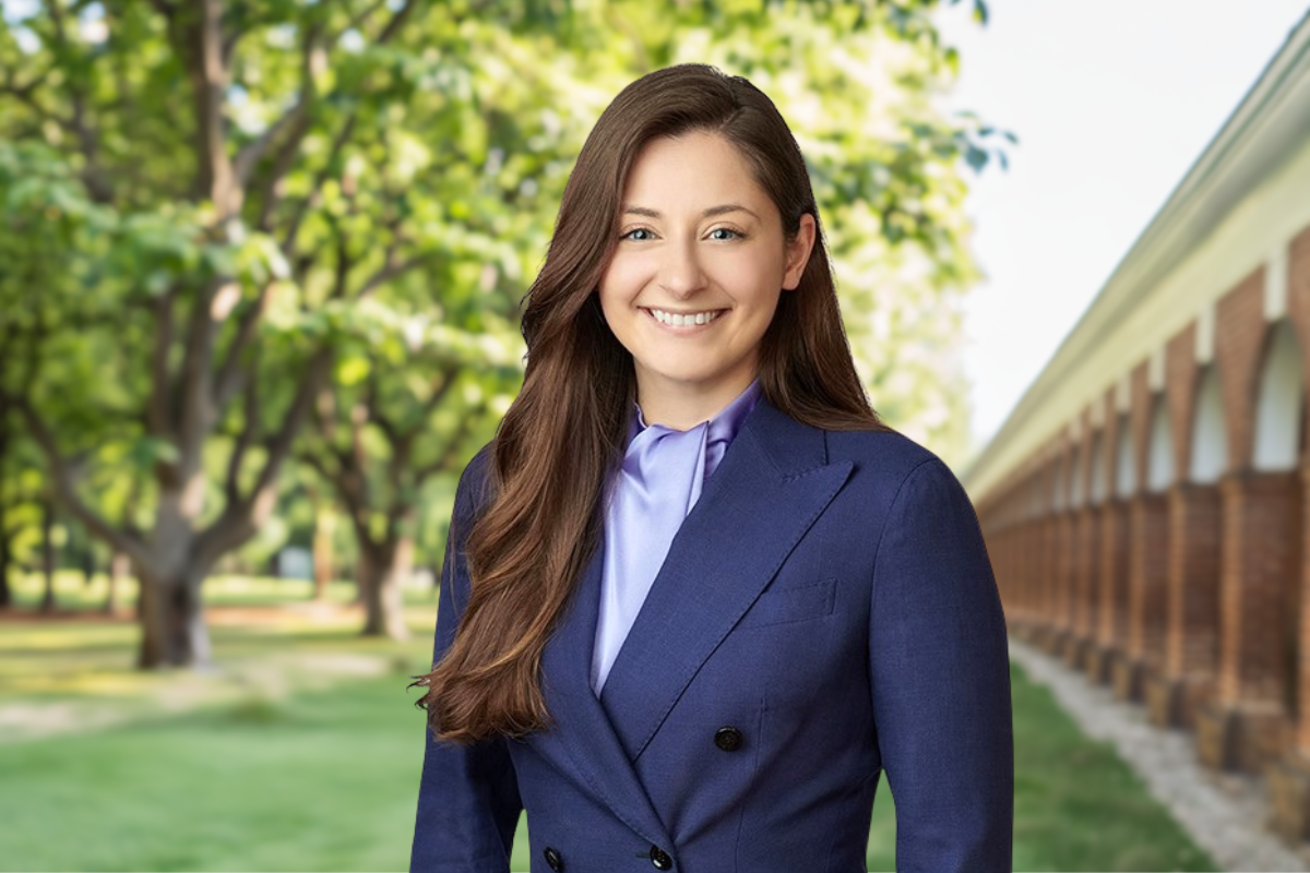Batten alumna Hayley Lawrence smiles at the camera in a blue blazer with the UVA campus colonnades in the background